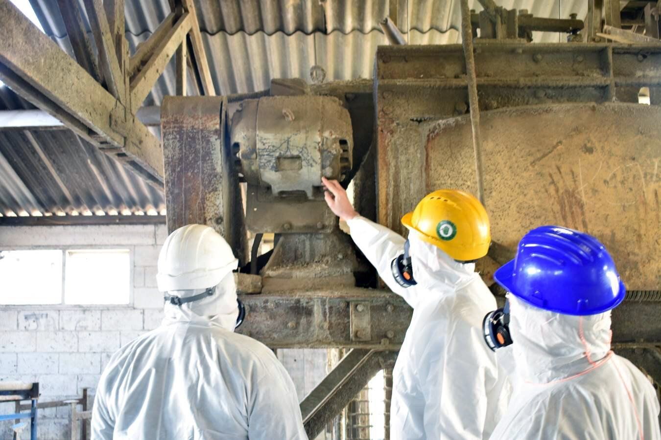 Three workers in hard hats inspect machinery inside an industrial plant.