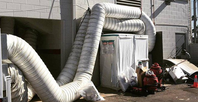 Large white ventilation ducts connected to a building, with equipment and debris outside in a utility area