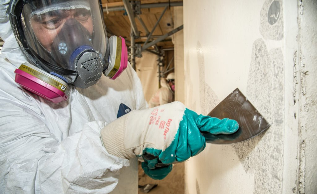 Worker in respirator smoothing plaster on a wall with a trowel indoors