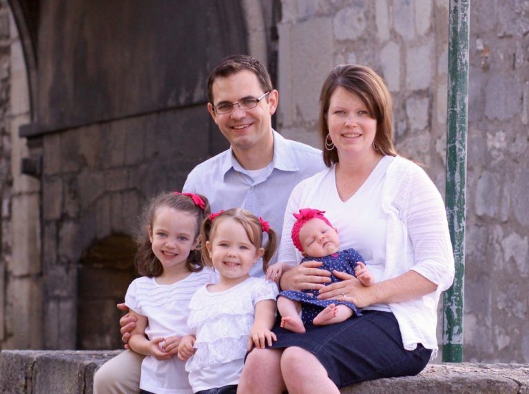 A family is posing for a picture while sitting on a stone wall.
