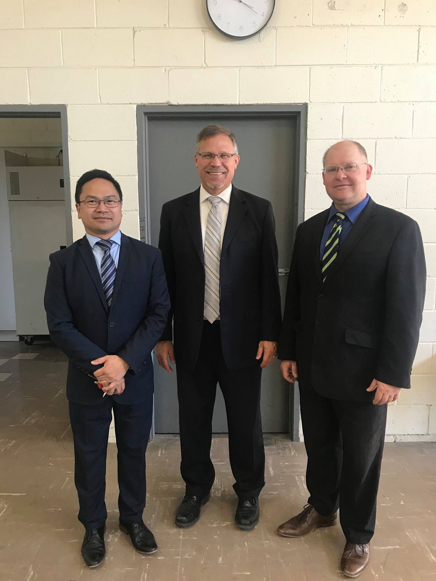 Three men in suits and ties are standing next to each other in front of a door.