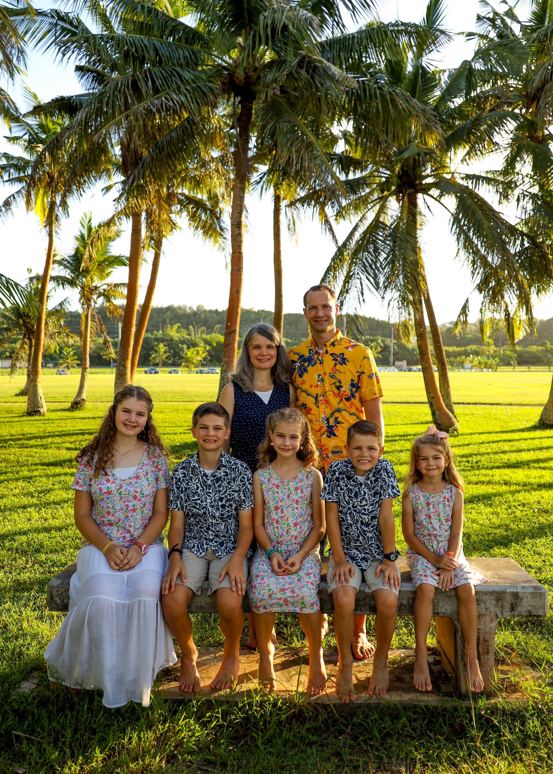 A family is posing for a picture while sitting on a bench under palm trees.