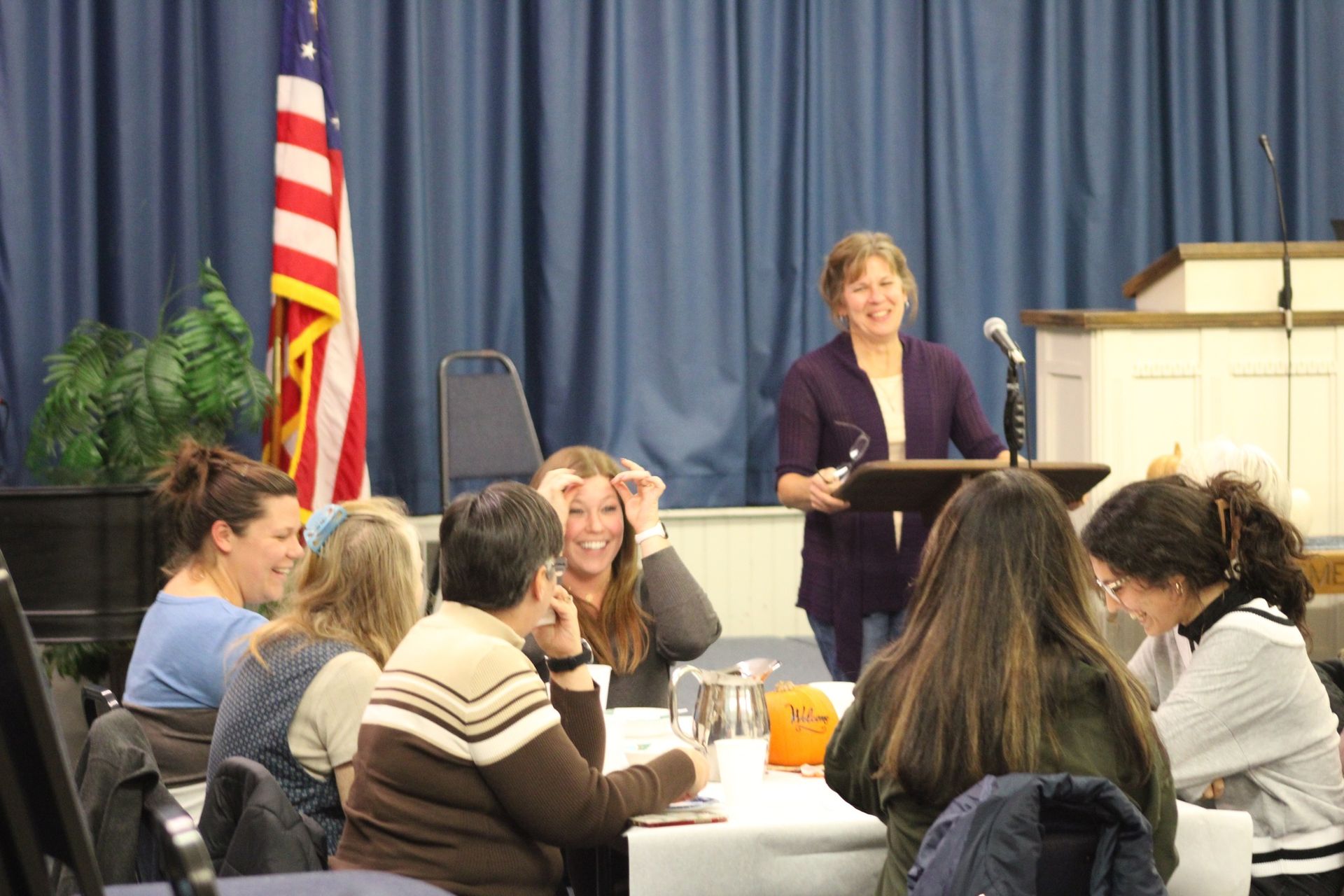 A woman is giving a speech to a group of people sitting at a table.