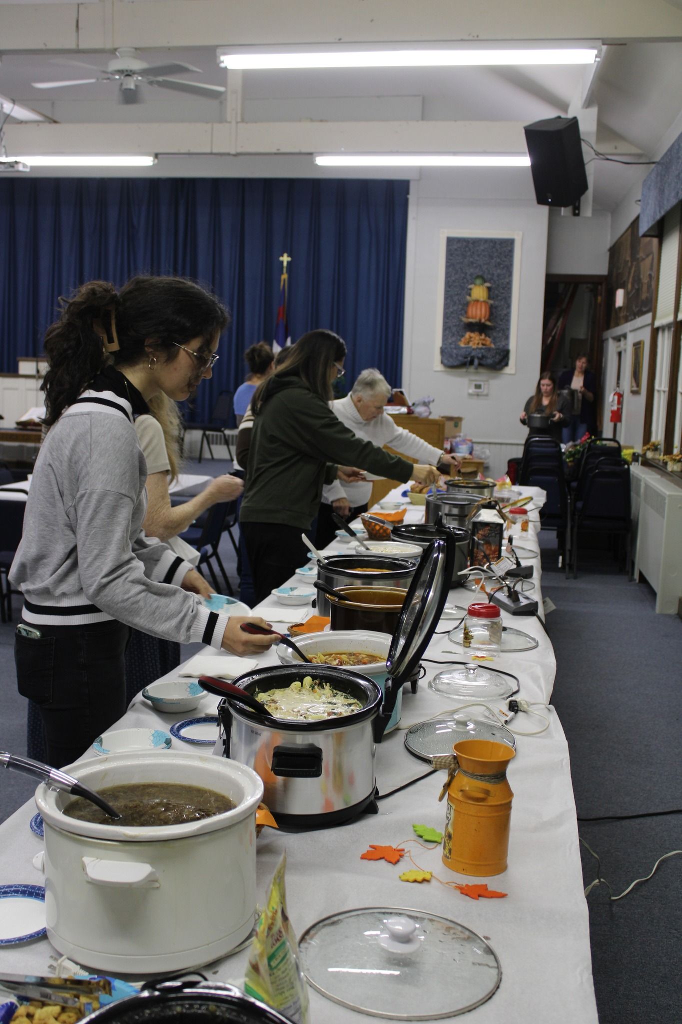 A group of people are standing around a long table with pots of food.