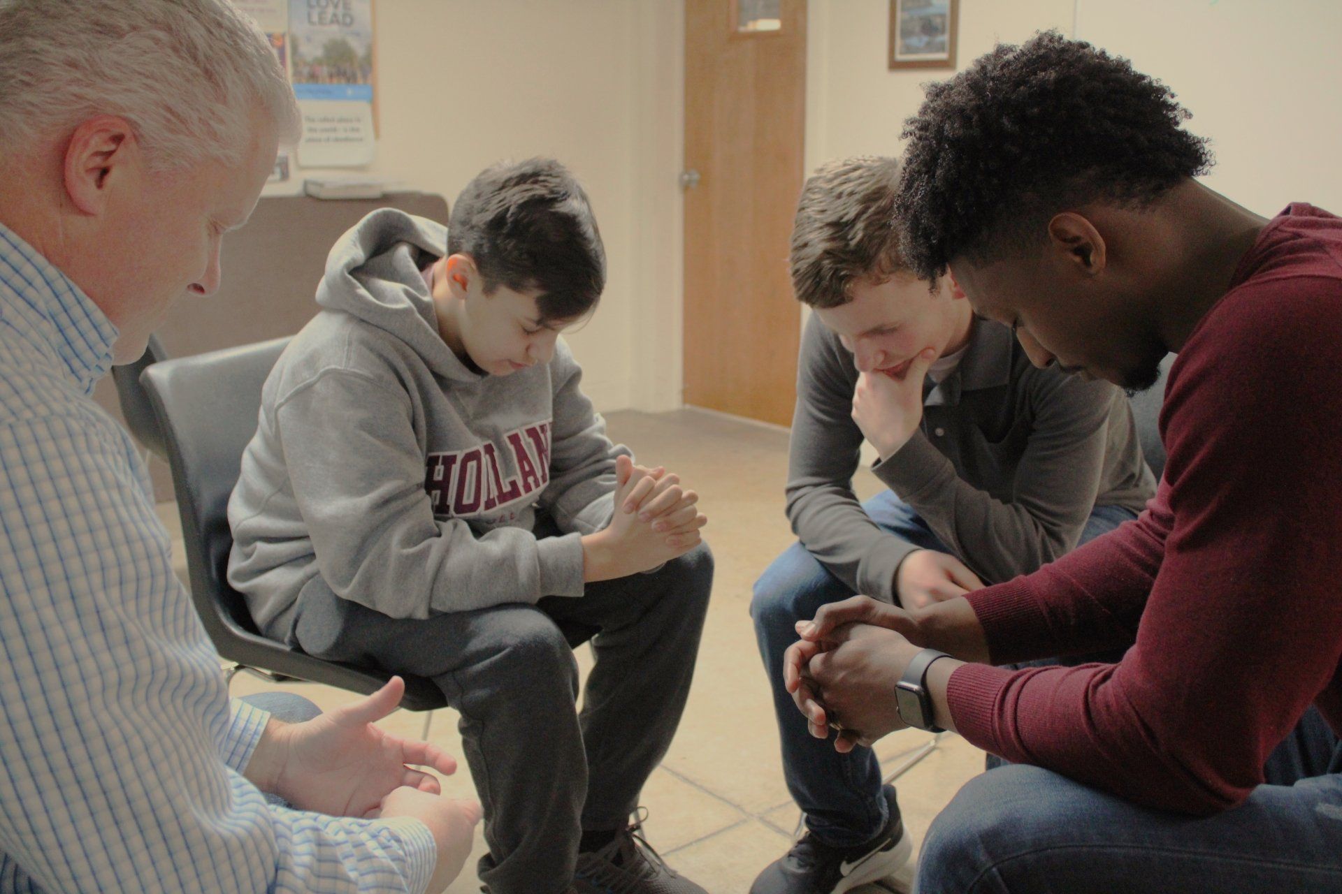 A group of young men are sitting in a circle with their hands folded in prayer.
