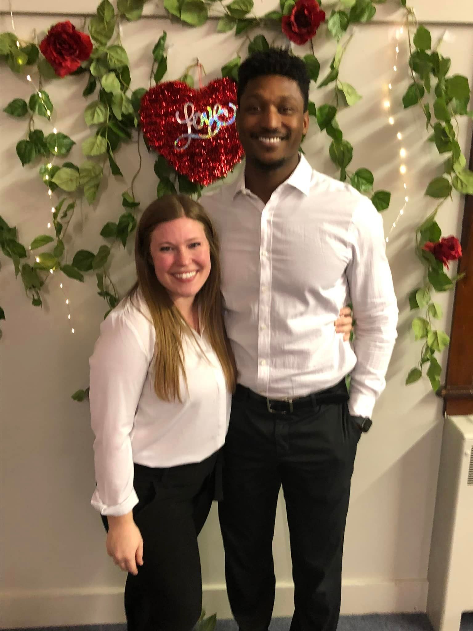 A man and a woman are posing for a picture in front of a heart shaped balloon.