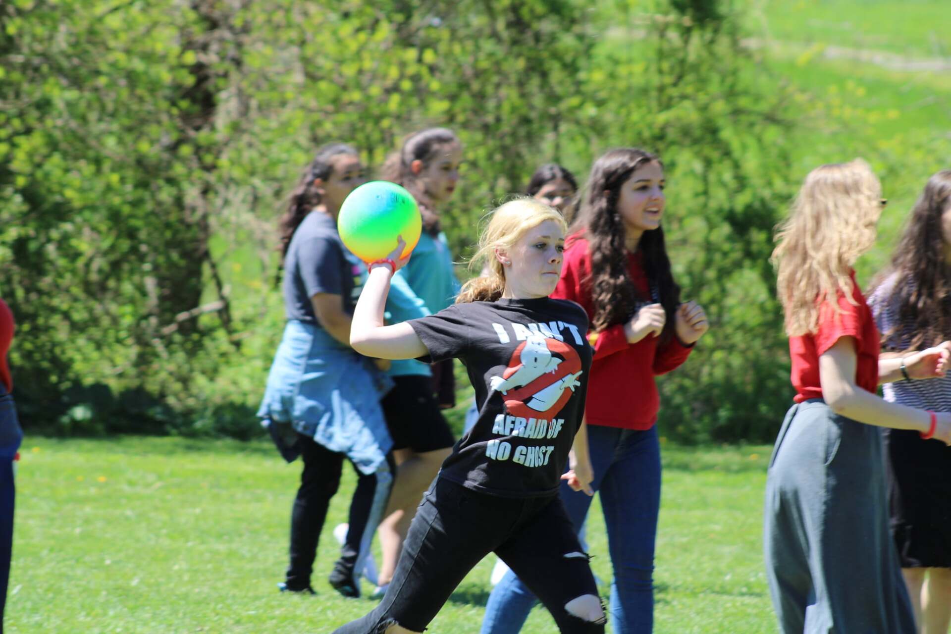 A girl in a rolling stones shirt is throwing a ball in a field.