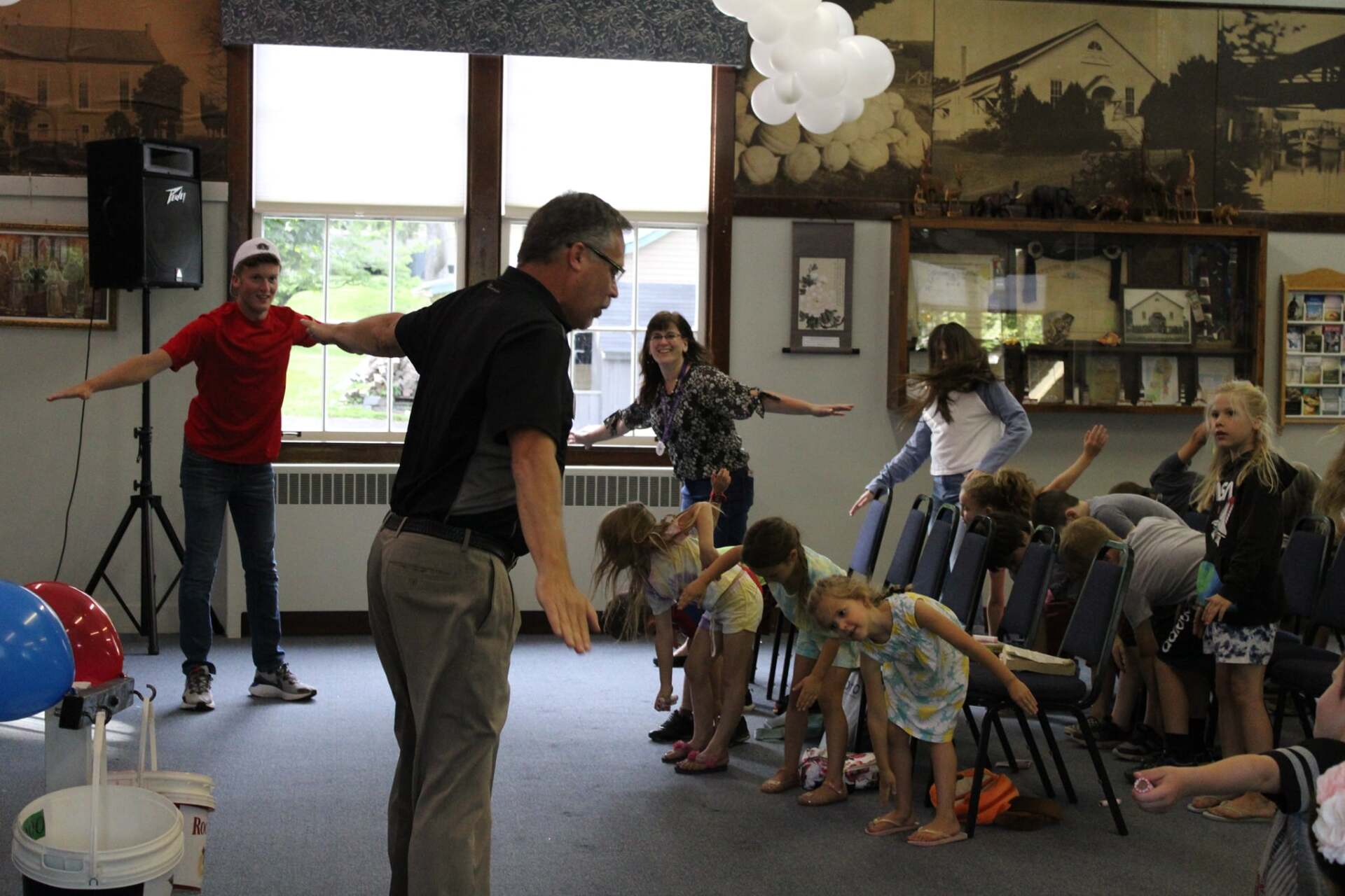 A man is standing in front of a group of children doing stretching exercises