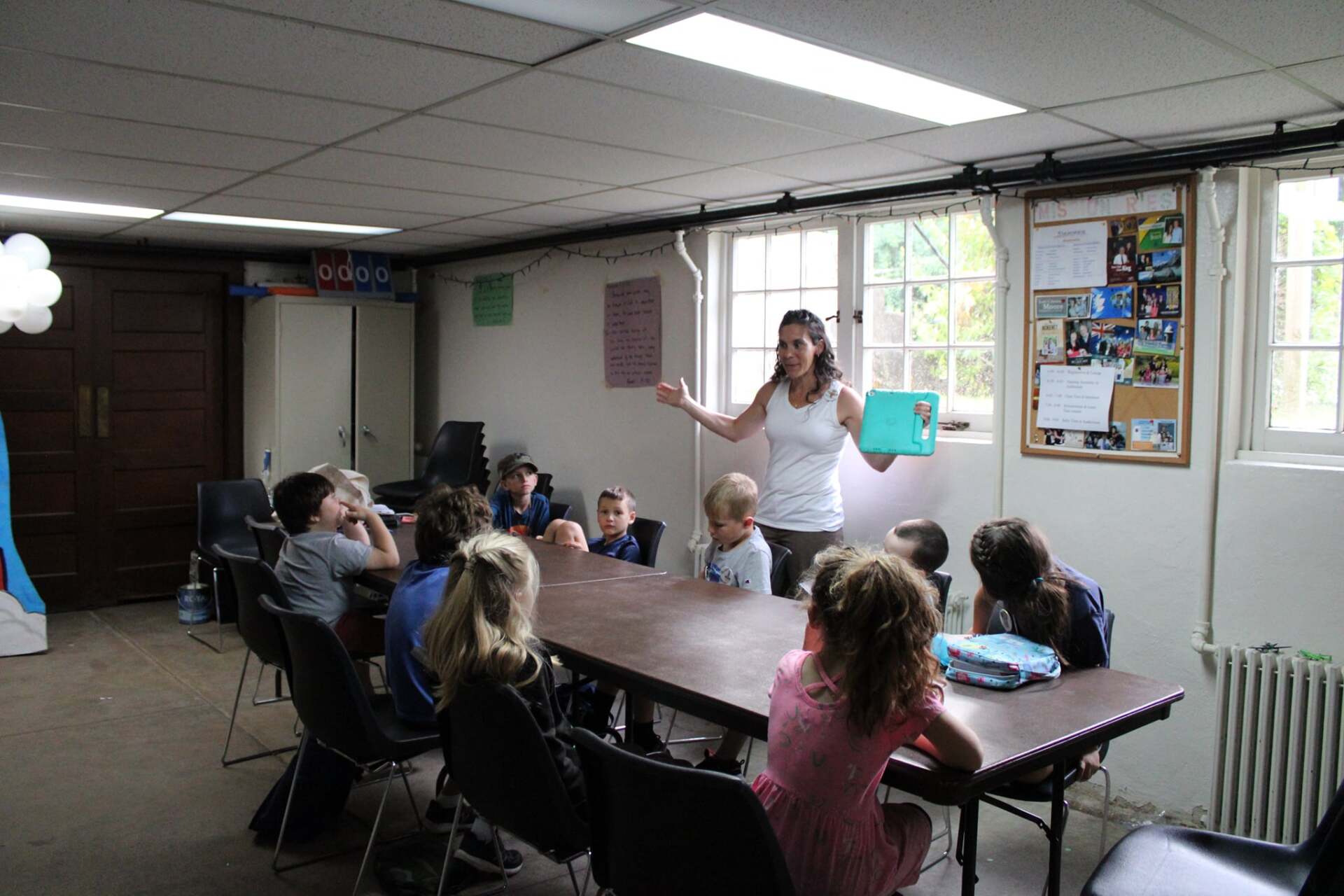 A woman is giving a presentation to a group of children sitting around a table.