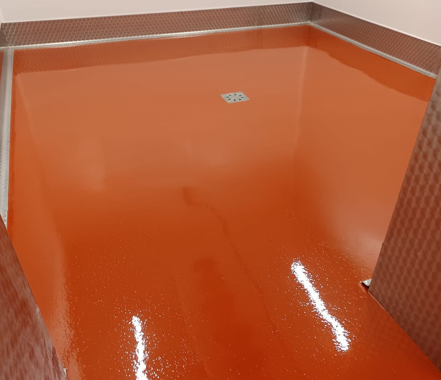 Pavimento rosa punteggiato in una stanza stretta con pareti bianche e una finestra in fondo.