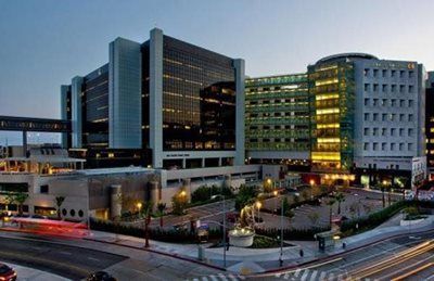 Modern hospital campus at dusk with illuminated buildings and a busy street in the foreground