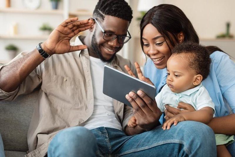 Family on a couch looking at a tablet, smiling and waving together