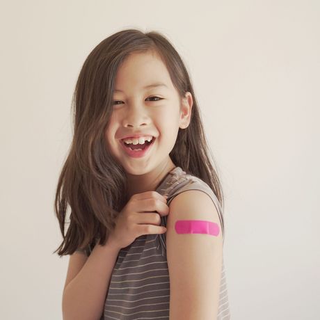 Smiling child showing a pink bandage on their upper arm against a light background