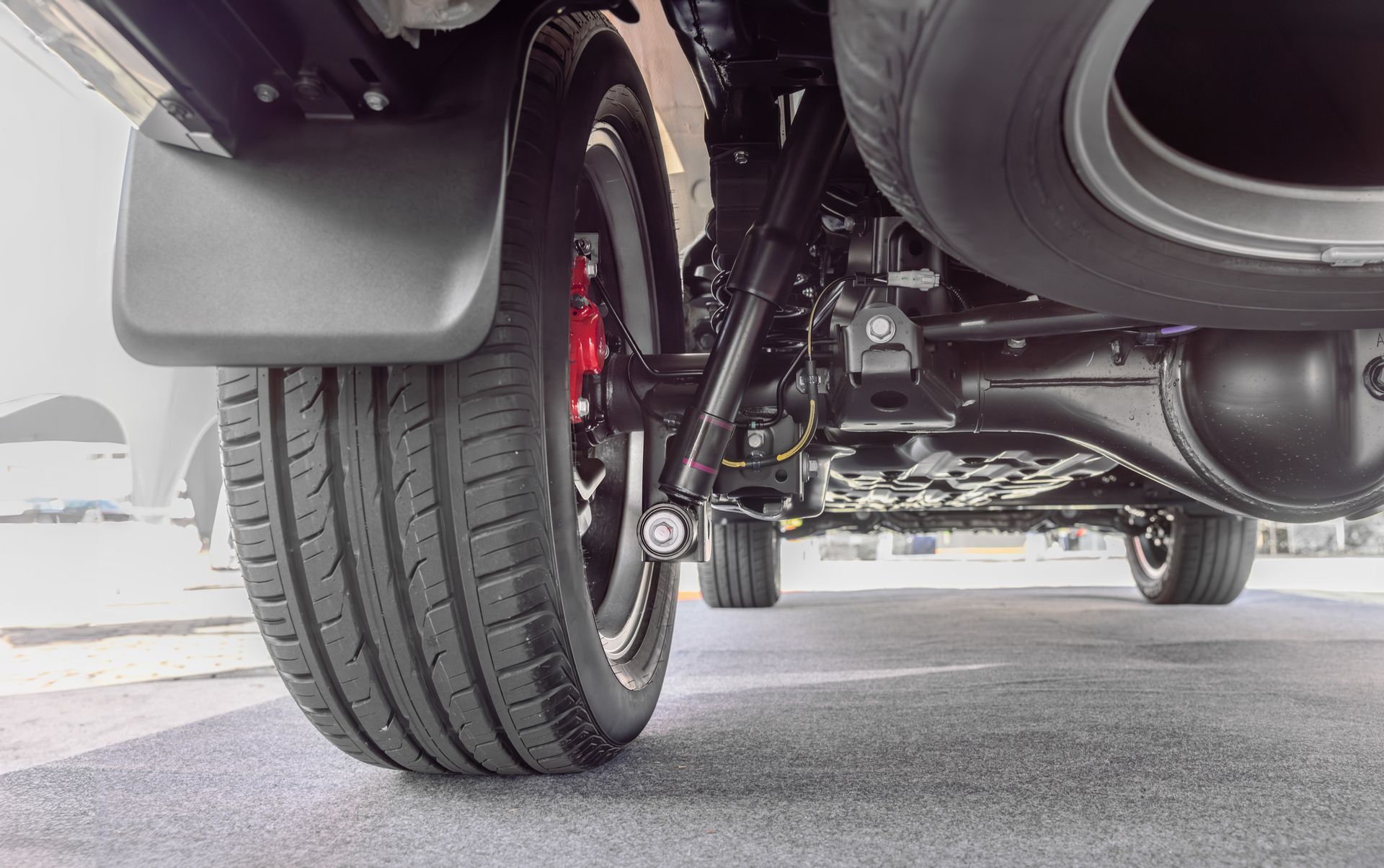 Underside of a vehicle with a tire and suspension visible. Black, gray, and red colors.