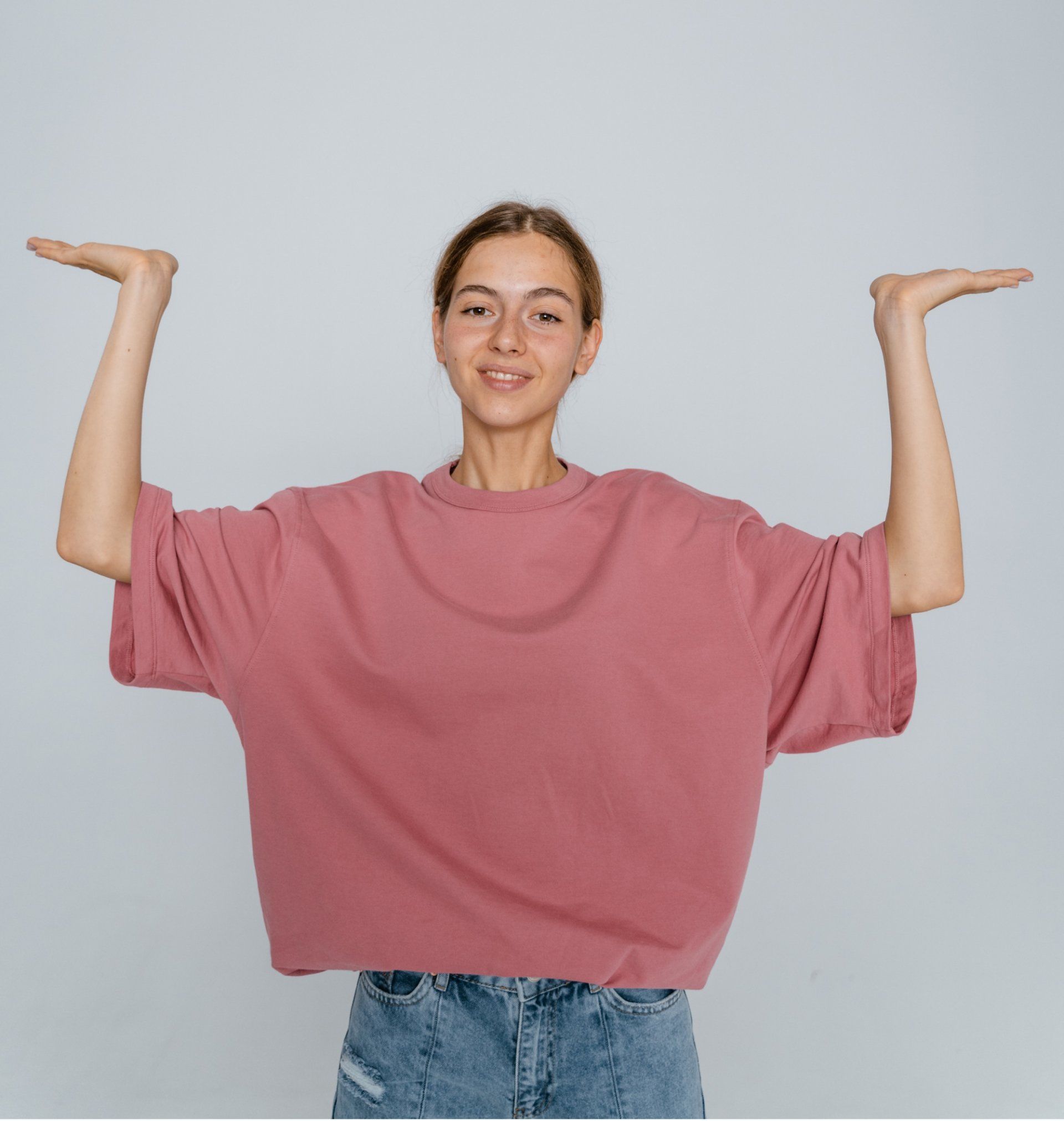 Woman wearing a rose-colored oversized t-shirt, light blue jeans, hands on hips, looking left.