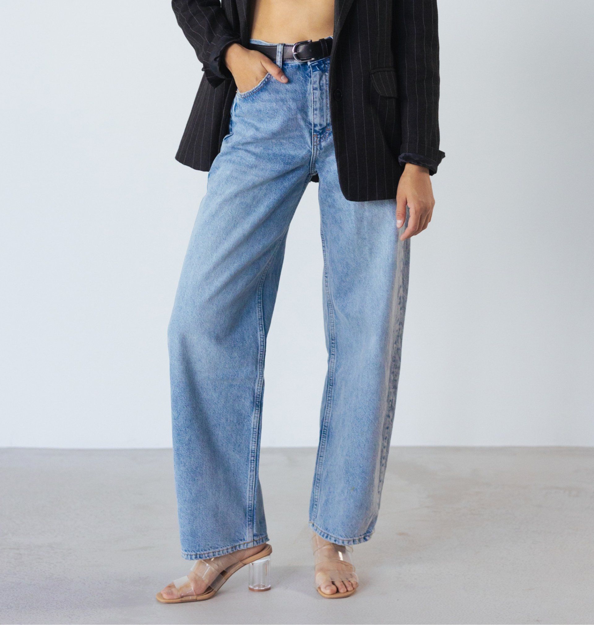 Woman wearing light wash denim jeans, black blazer, and clear heels.