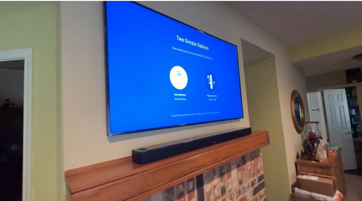 TV screen displays a setup screen, mounted above a fireplace with a sound bar.