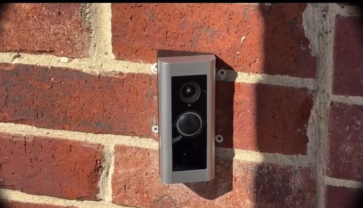 Ring doorbell on a red brick wall, capturing video and audio for security.