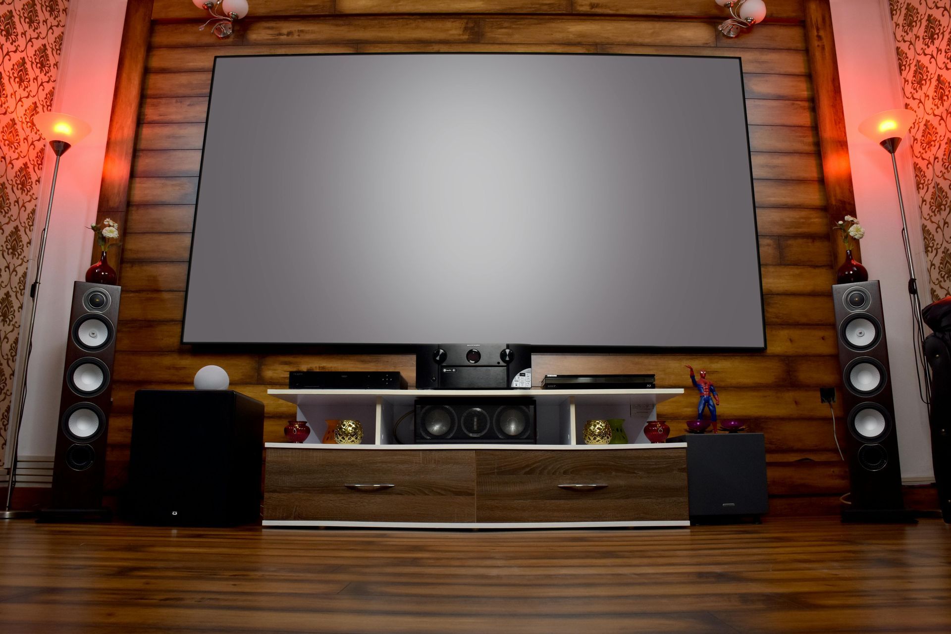 Home theater setup with large screen, speakers, and media console in a wooden-paneled room.