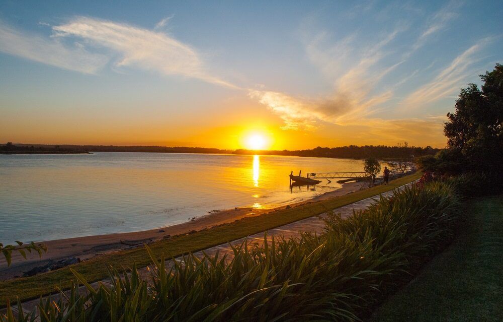 A Sunset Over a Lake with A Boat in The Water In Taree — D-Scapes Landscaping Services Pty Ltd in Forster, NSW 