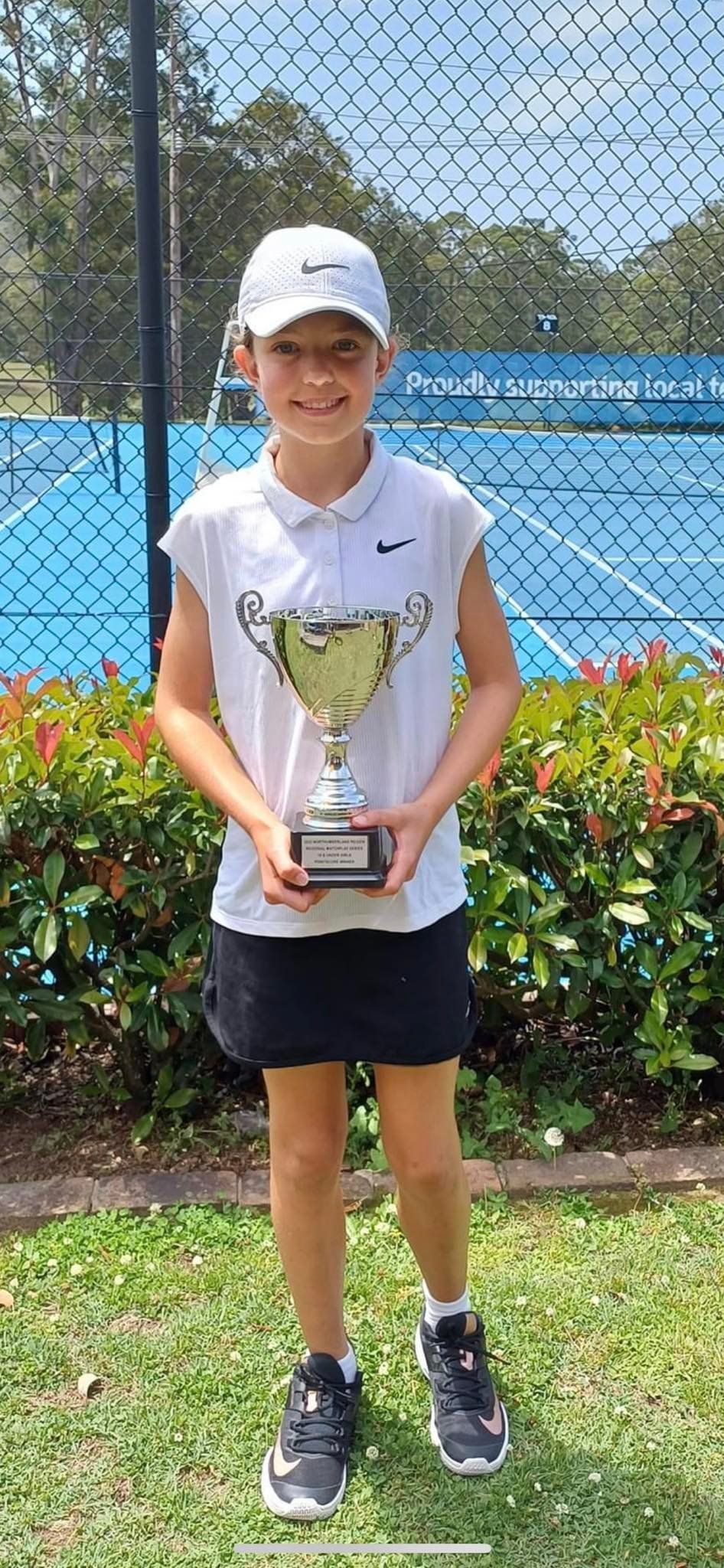 A Young Person Wearing a White Hat and Shirt Holding a Trophy on a Tennis Court — Topspin Tennis Newcastle in Lambton, NSW