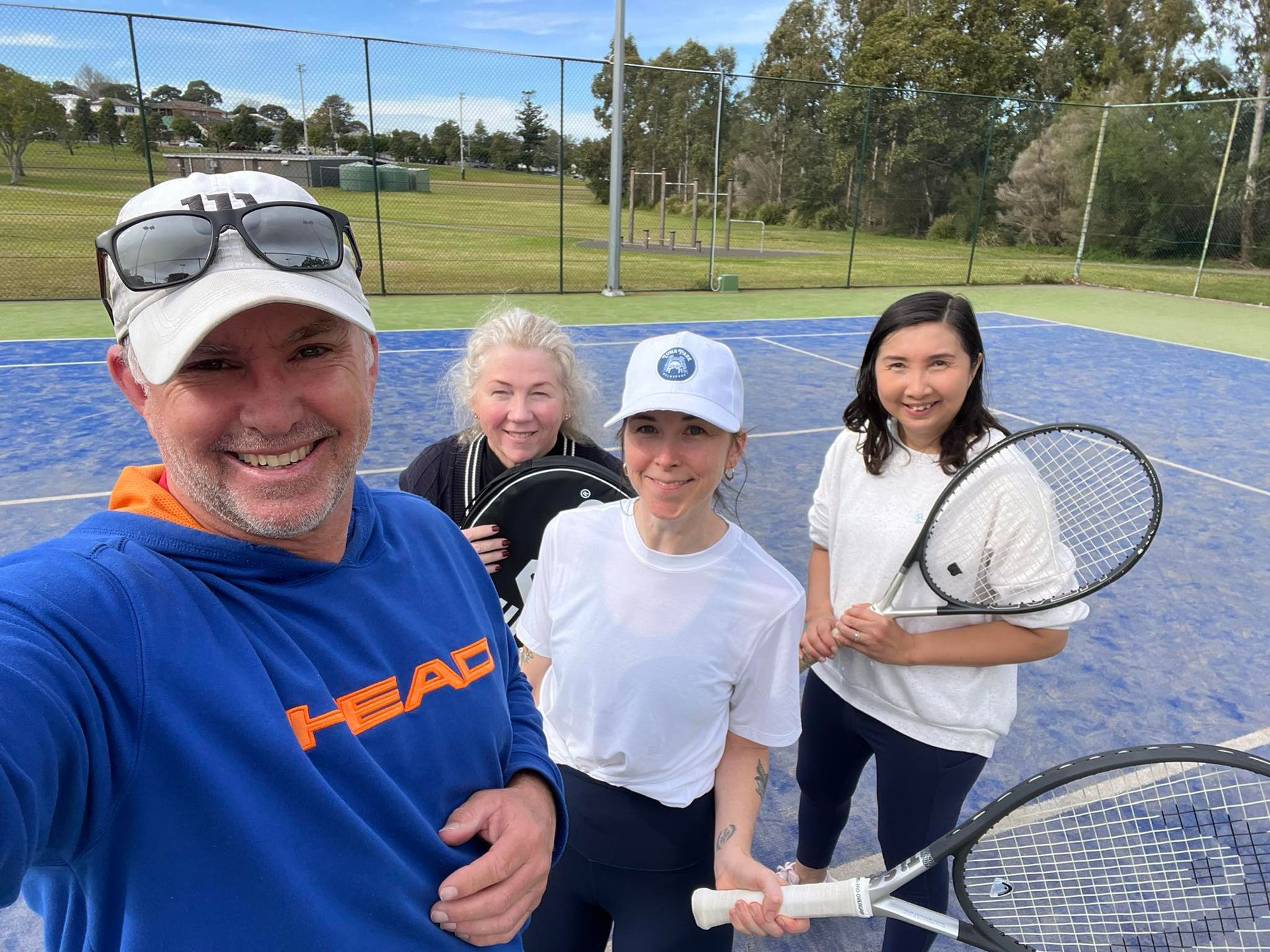 Four People Smile, Holding Tennis Rackets on a Blue Court — Topspin Tennis Newcastle in Adamstown, NSW
