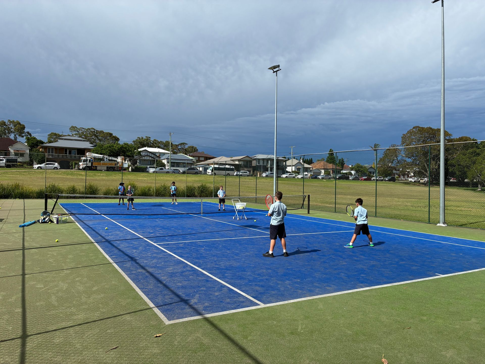 Tennis Players on a Blue Court, Playing a Match Outdoors Under a Cloudy Sky — Topspin Tennis Newcastle in Adamstown, NSW