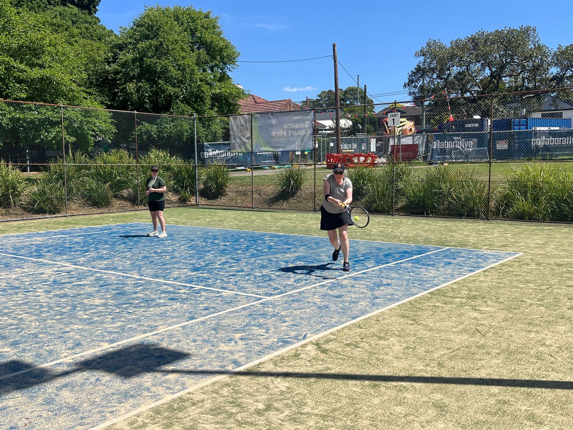 Two People Playing Tennis on a Blue Court, Green Surroundings — Topspin Tennis Newcastle in Lambton, NSW