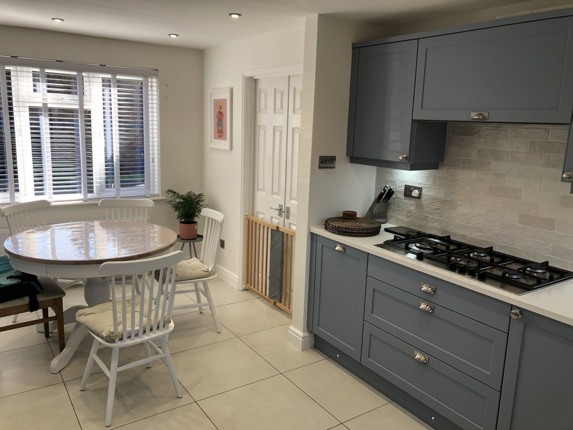 A bright, modern kitchen and dining area with grey cabinets, a gas stove, a round table with chairs, and a baby gate.