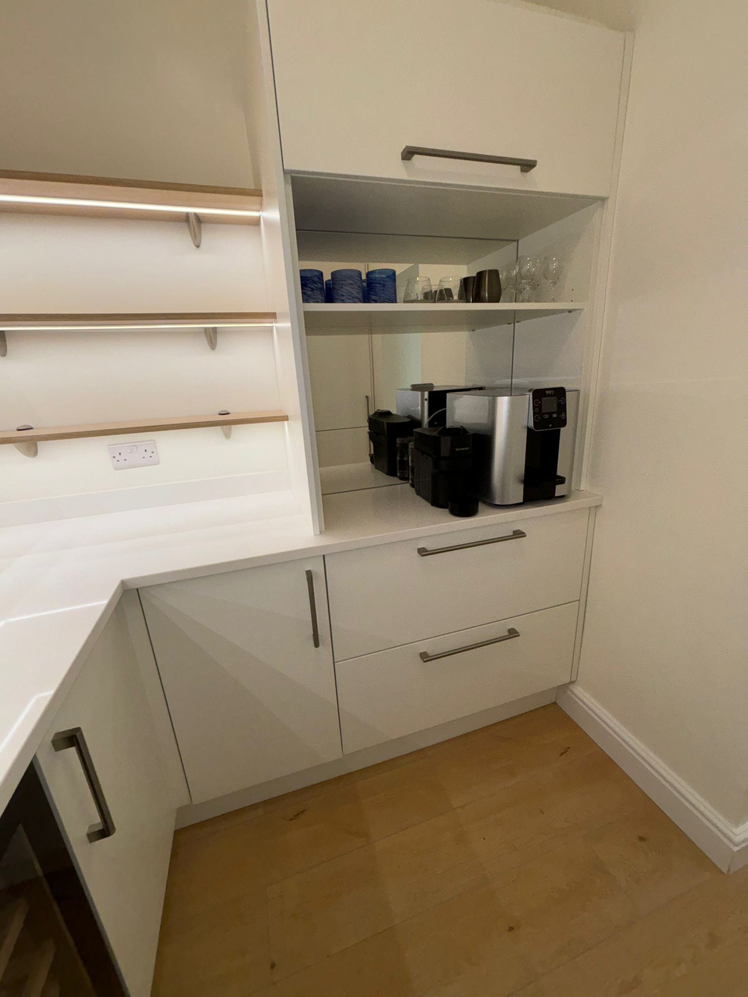 A white kitchen coffee station featuring open shelving, a coffee machine, and two drawers with silver handles.