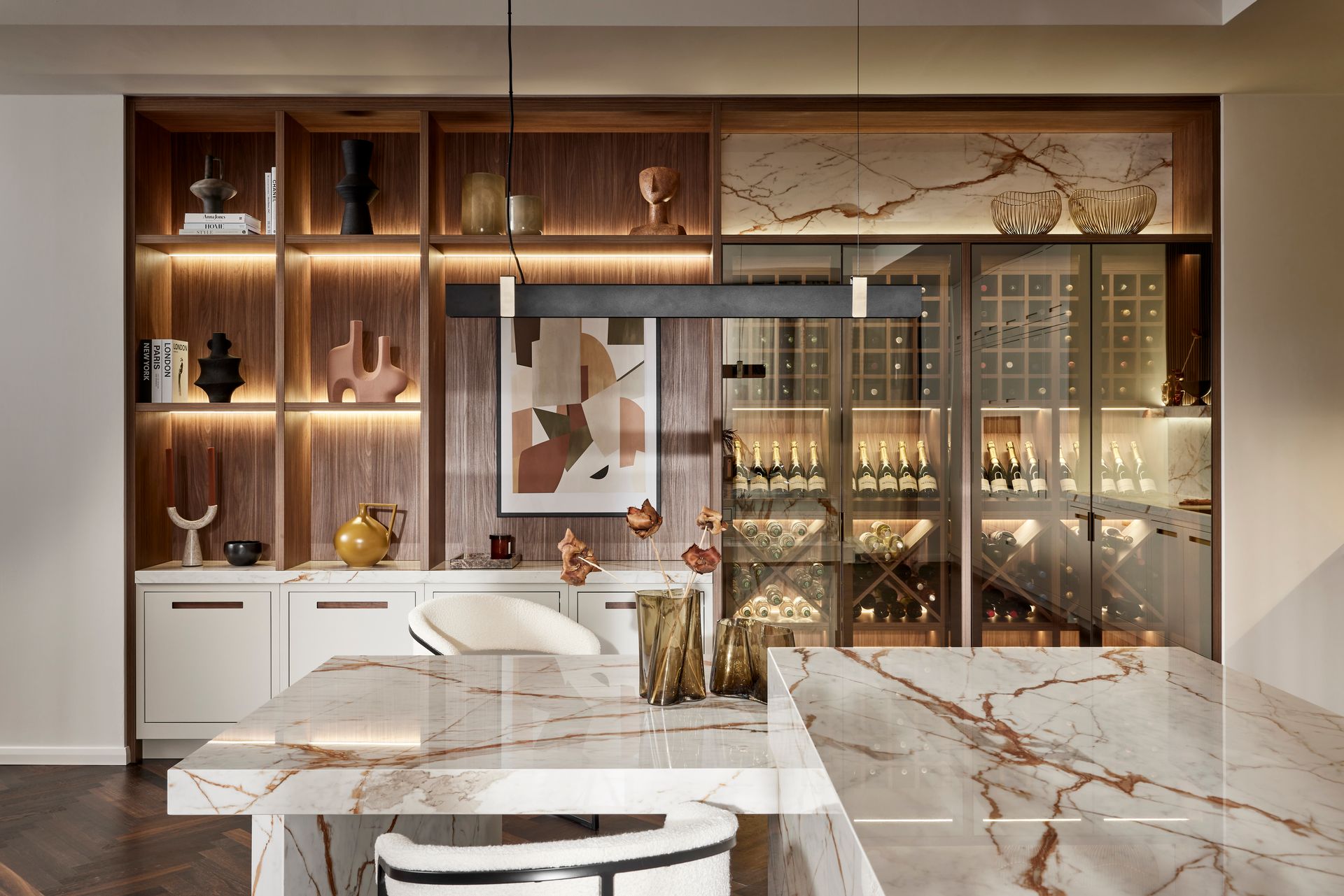 A modern dining area with a marble-topped table, white chairs, and an illuminated wood-shelved display with a wine cellar.