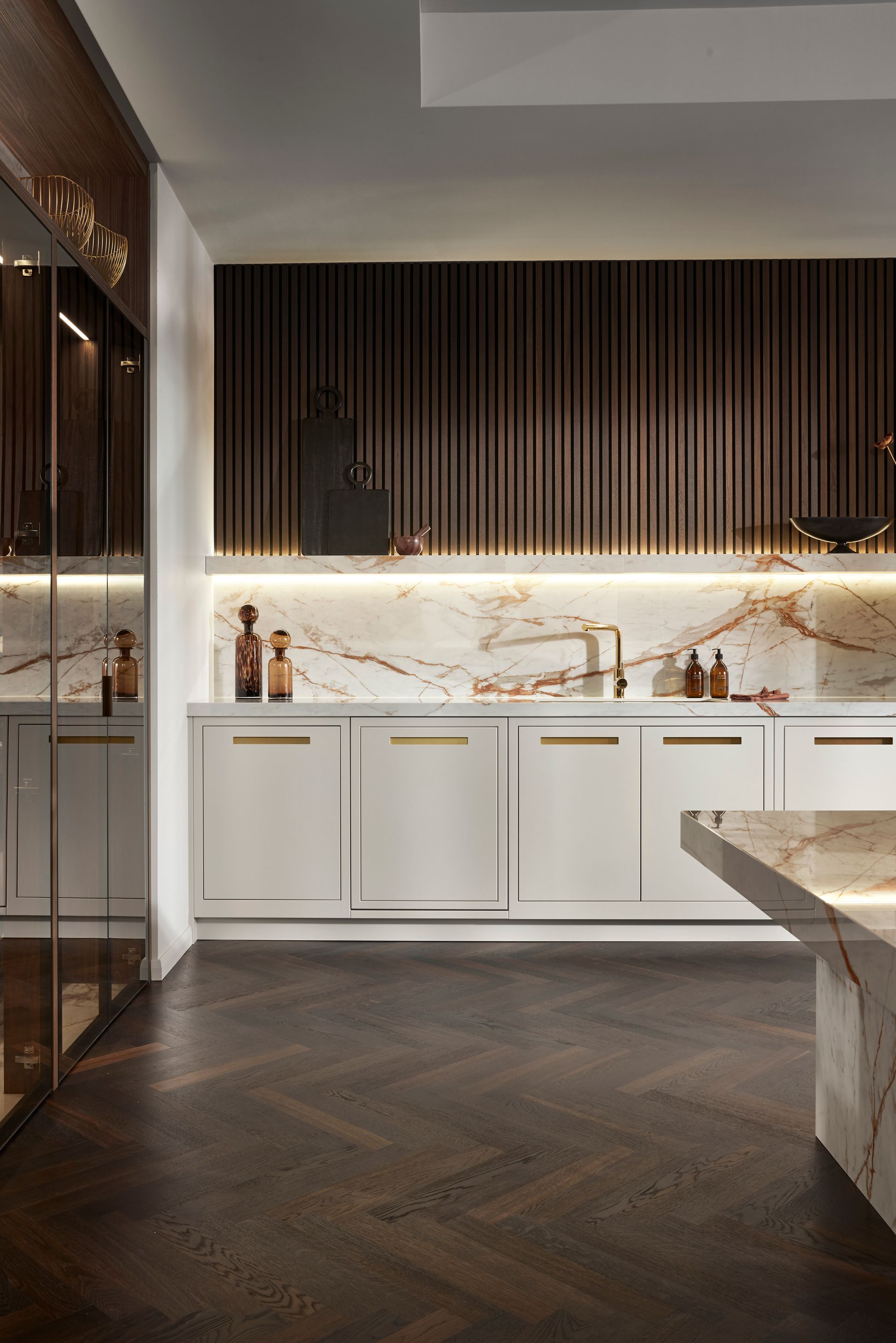 A modern kitchen with white cabinets, marble countertops, a marble backsplash, and a dark herringbone wood floor.