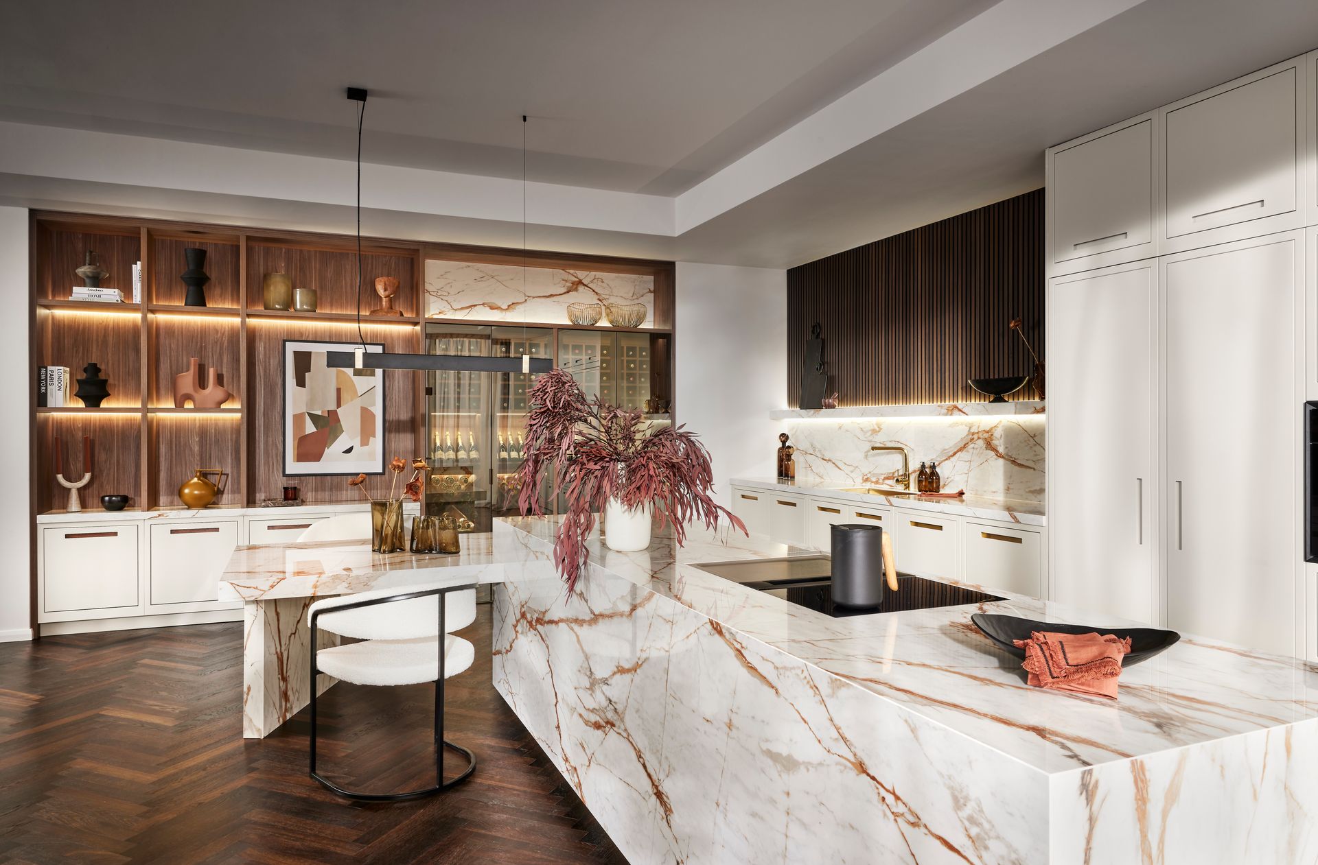 Modern kitchen with a large marble island, herringbone wood floors, white cabinets, and warm under-cabinet lighting.