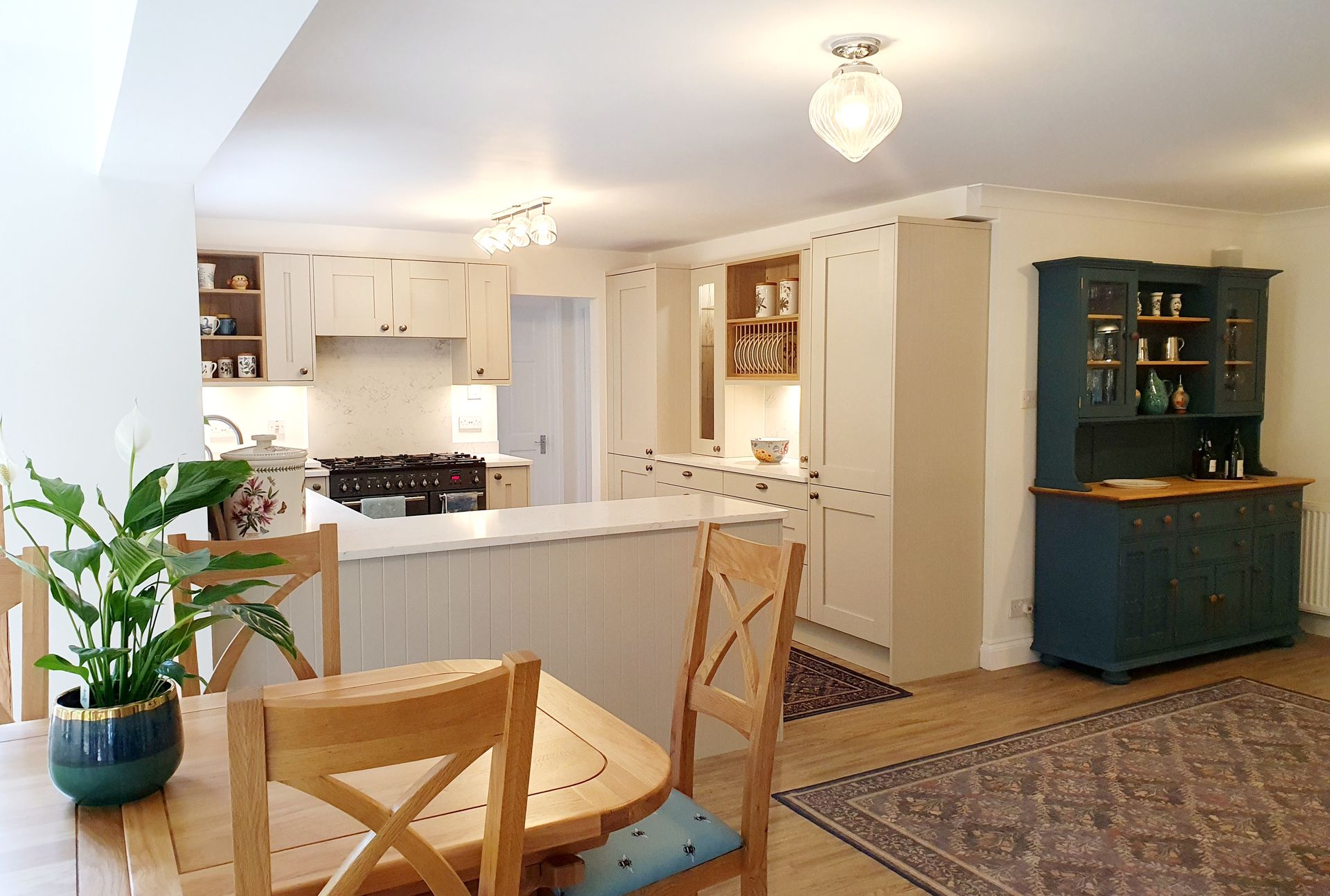 A bright open-plan kitchen with cream cabinetry, a breakfast island, a small wooden dining set, and a blue hutch.
