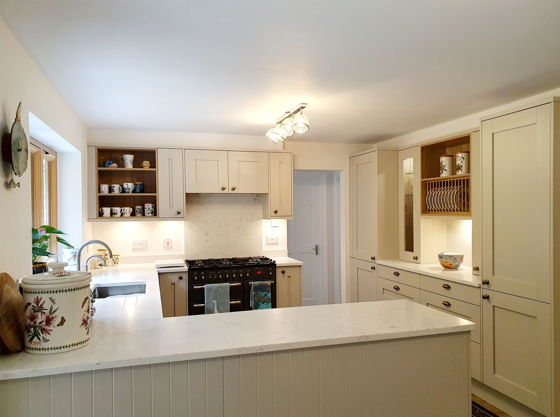 A bright, modern kitchen featuring cream-colored cabinets, a white marble countertop peninsula, and a central gas range.