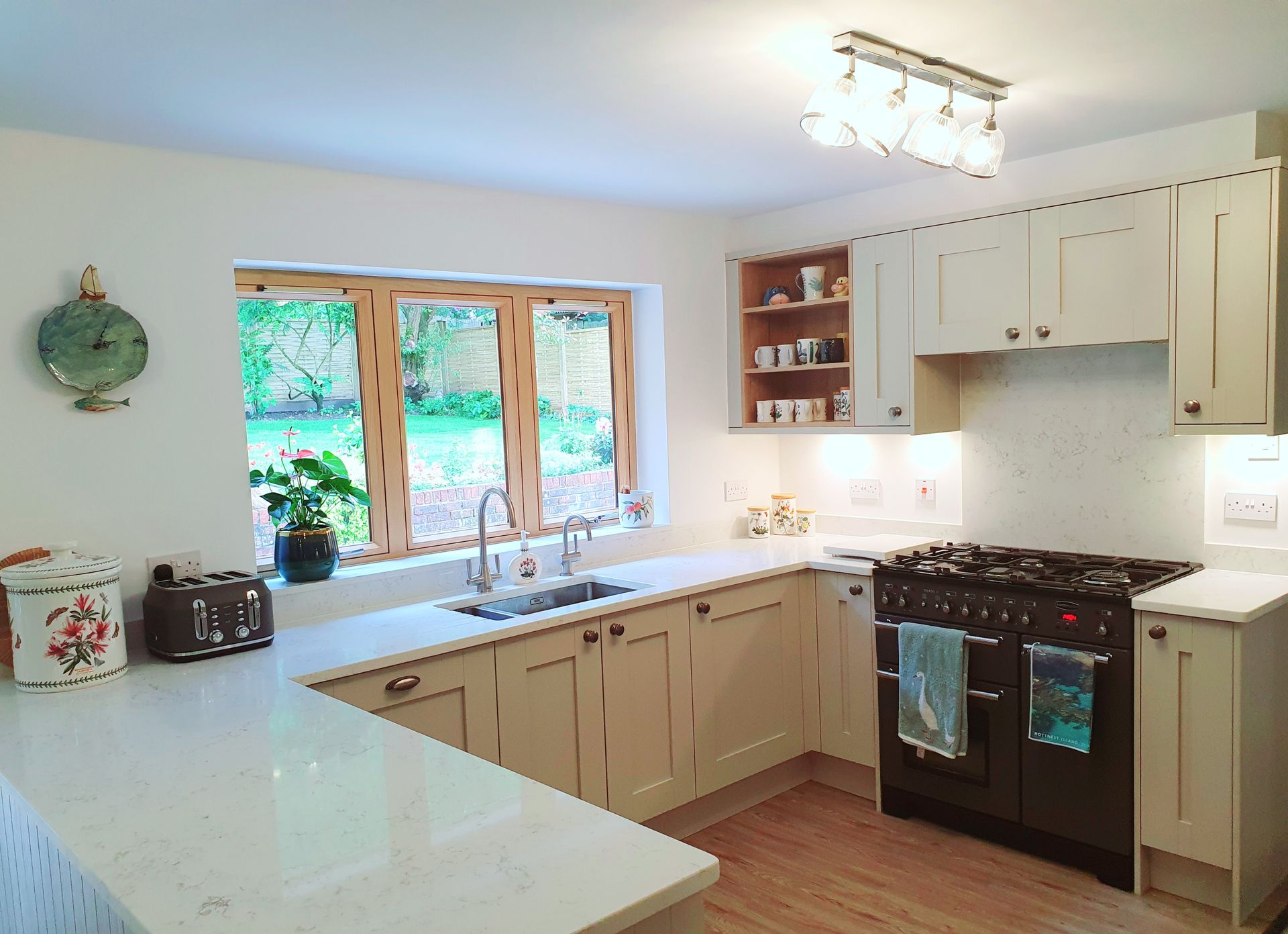 A bright kitchen with cream cabinets, a black range cooker, a window over the sink, and white countertops.
