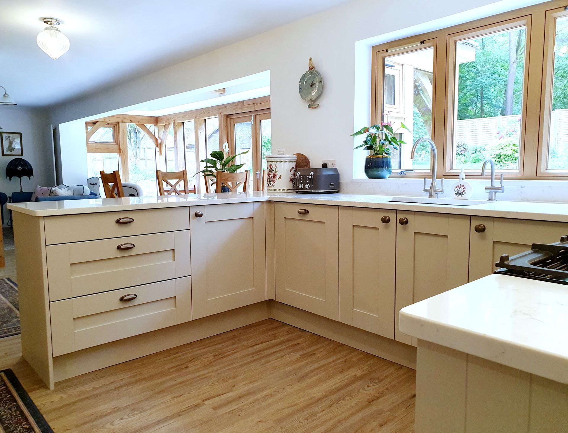 A bright kitchen with cream-colored cabinets, light wood flooring, and a large window overlooking a garden.