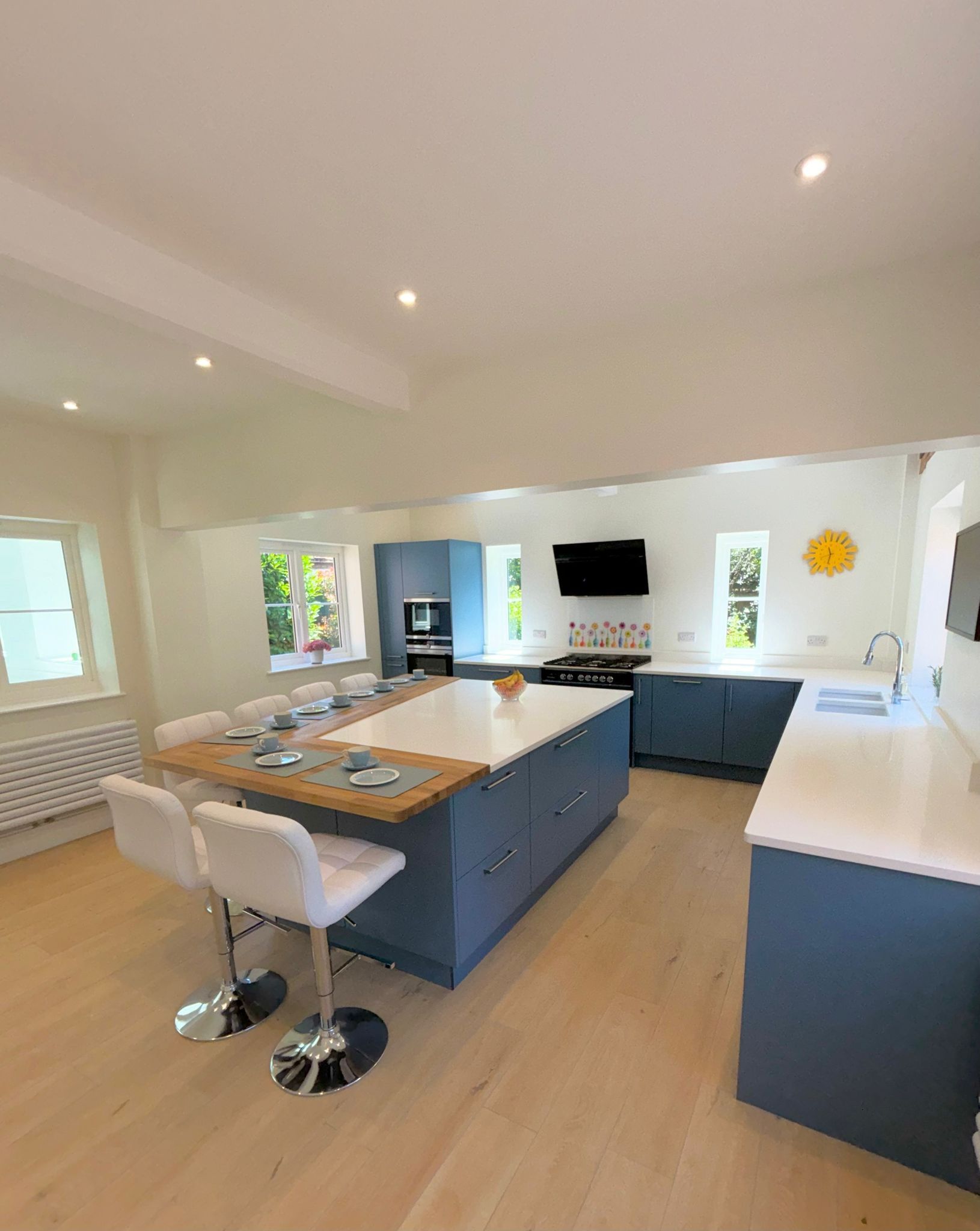 Modern kitchen with a blue island, wood-topped breakfast bar, white countertops, and light wood floors in a bright space.