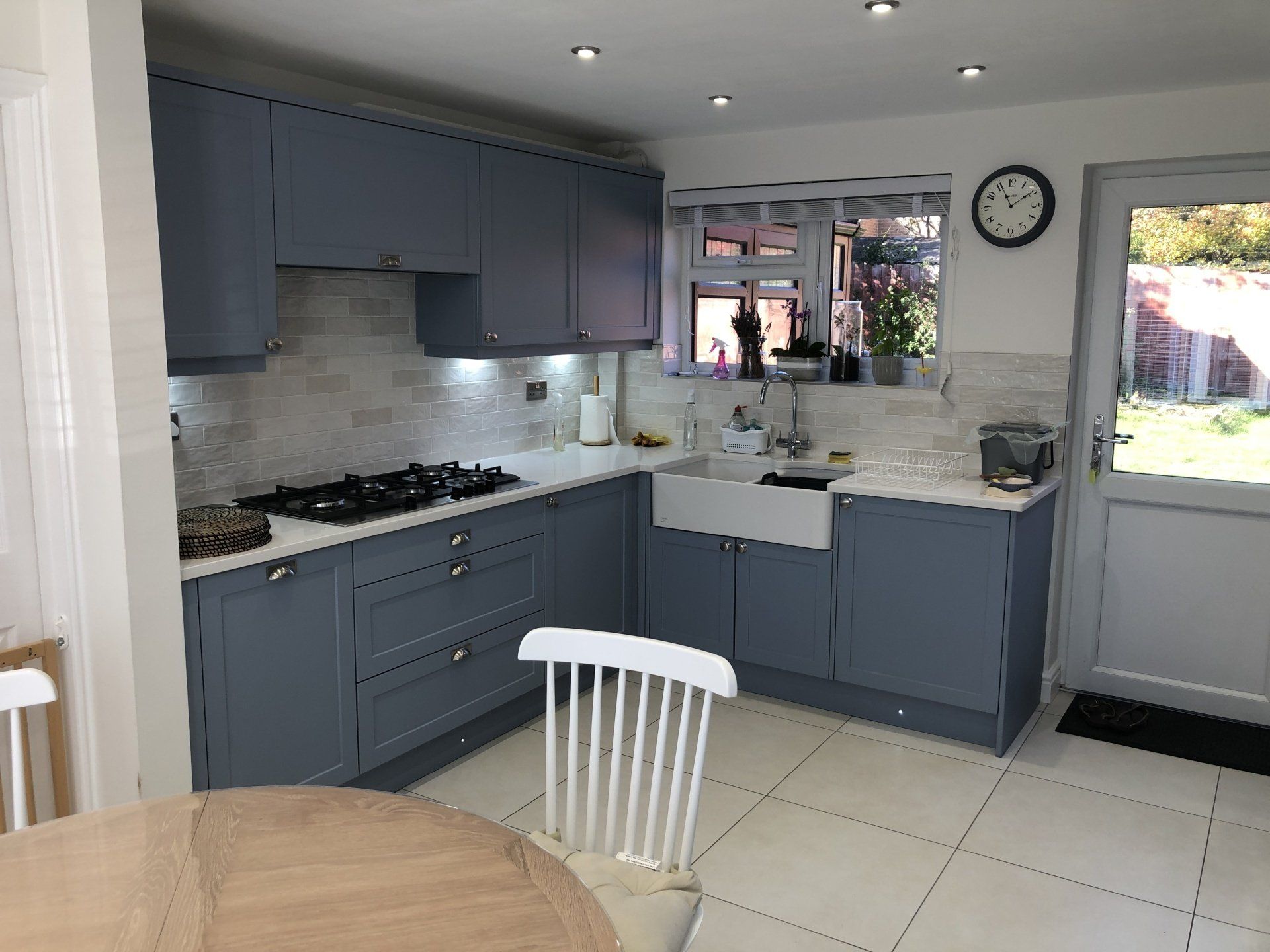 A kitchen with blue cabinets, white countertops, a farmhouse sink, and a gas stove, with a white chair in the foreground.