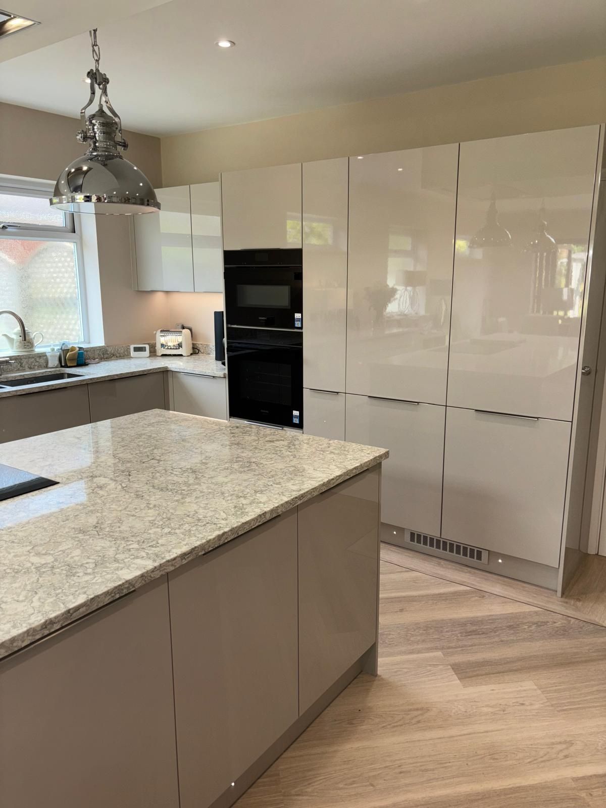 A modern kitchen featuring light beige cabinetry, a granite-topped island, a built-in oven, and light wood flooring.