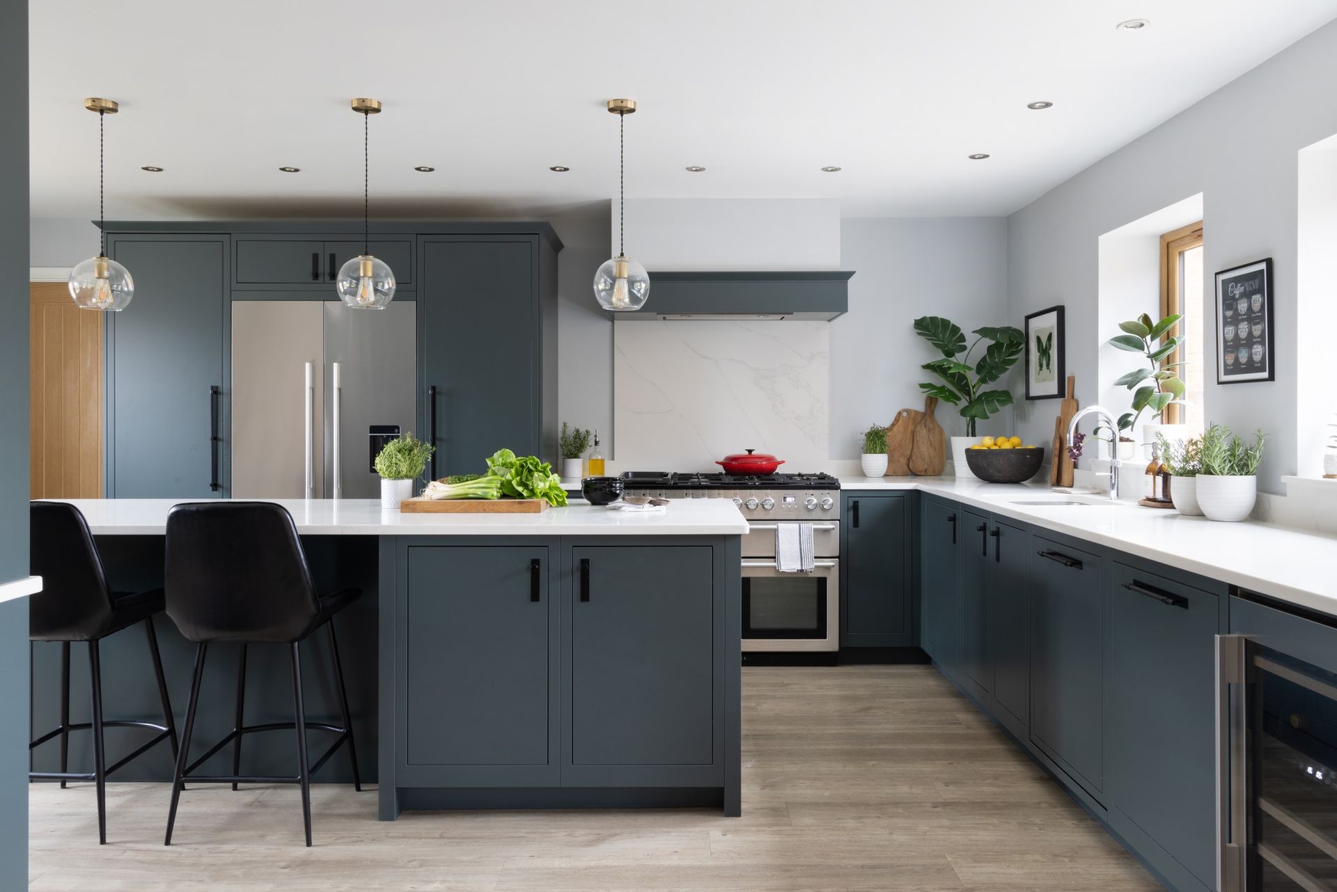 Modern kitchen with dark grey cabinetry, white countertops, an island with bar stools, and warm pendant lighting.