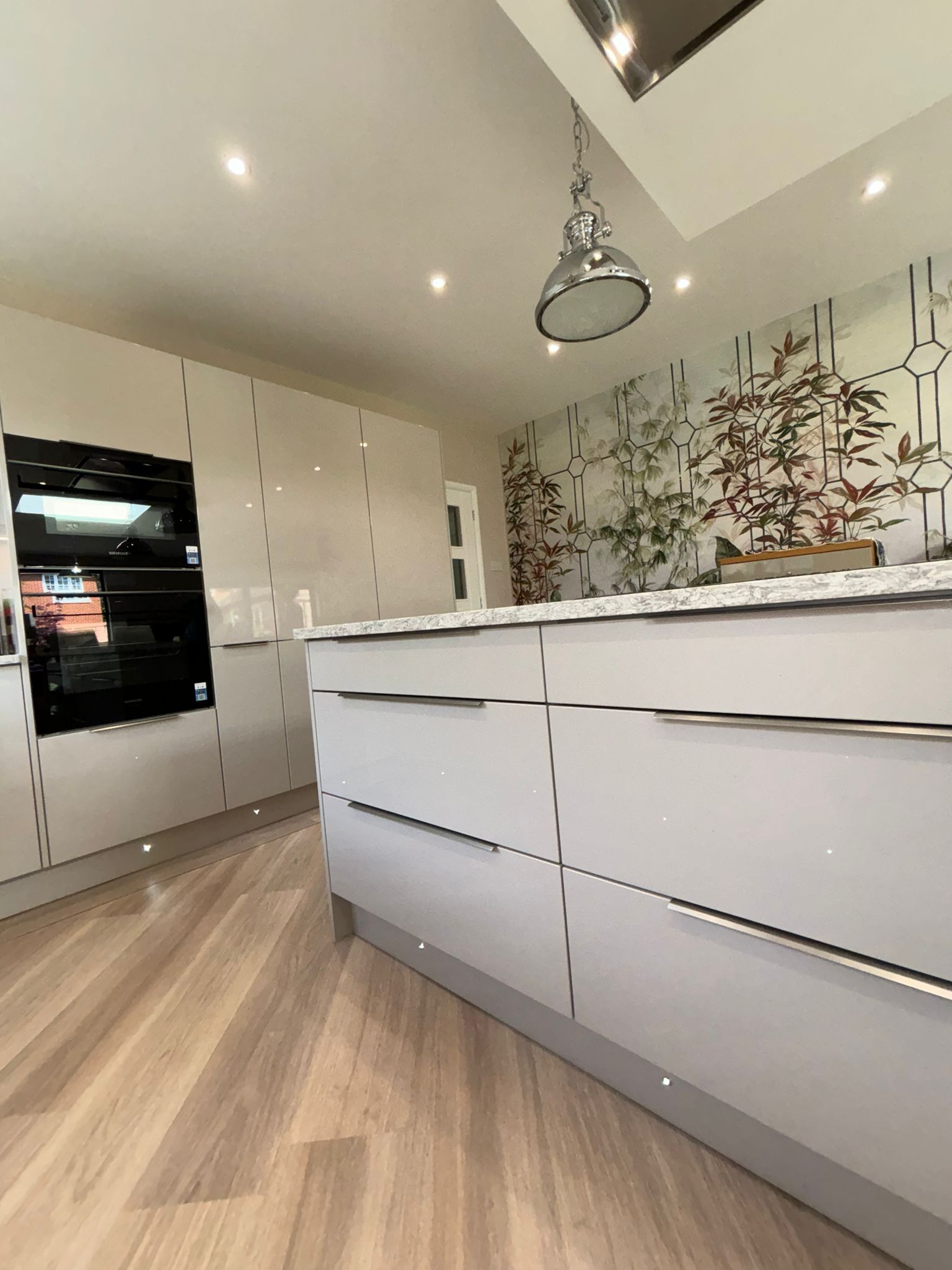 A modern kitchen with light gray cabinetry, a large kitchen island, stainless steel appliances, and wood-patterned flooring.