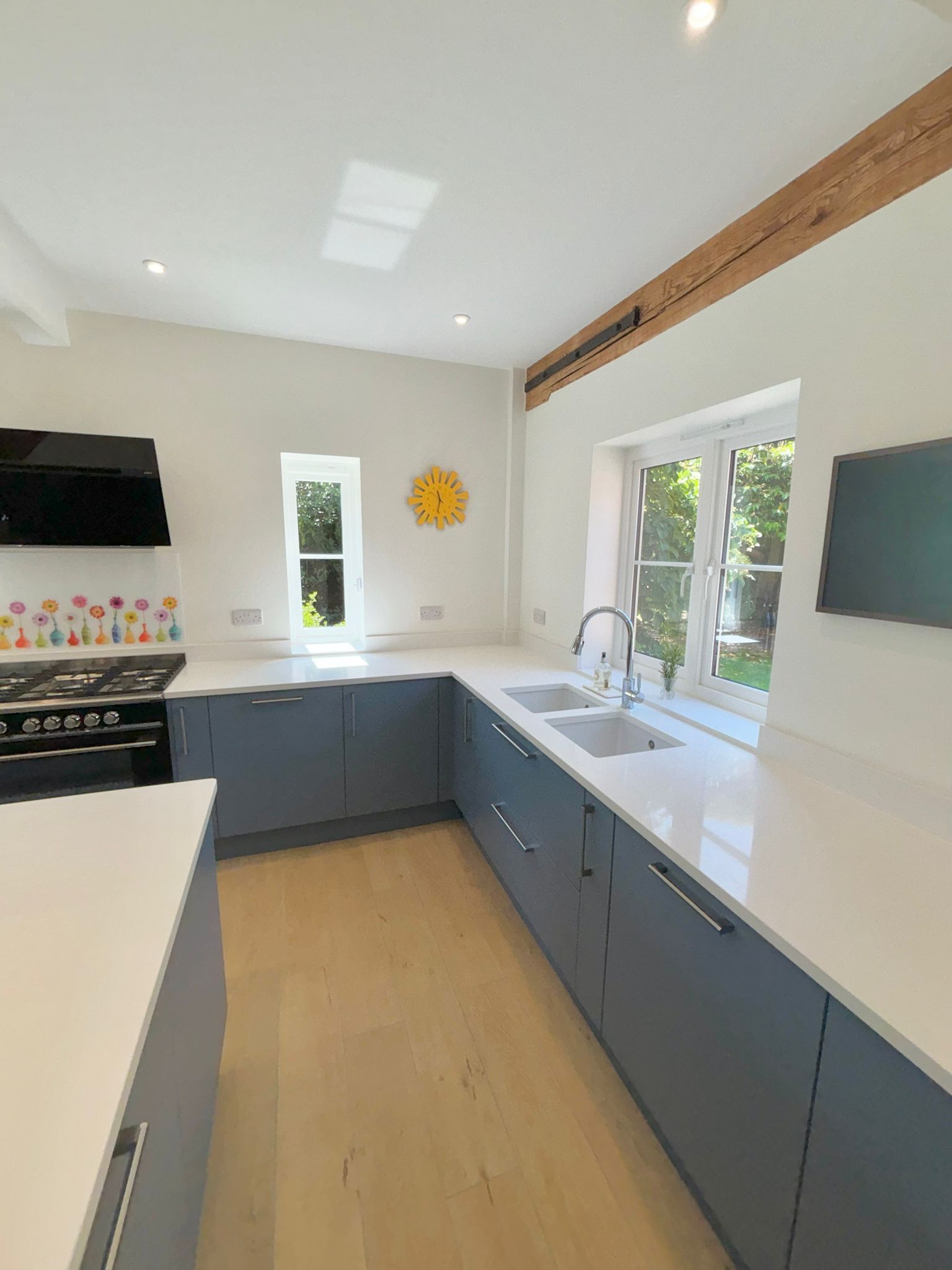A modern kitchen with grey cabinets, white countertops, light wood floors, and a bright window over a double sink.