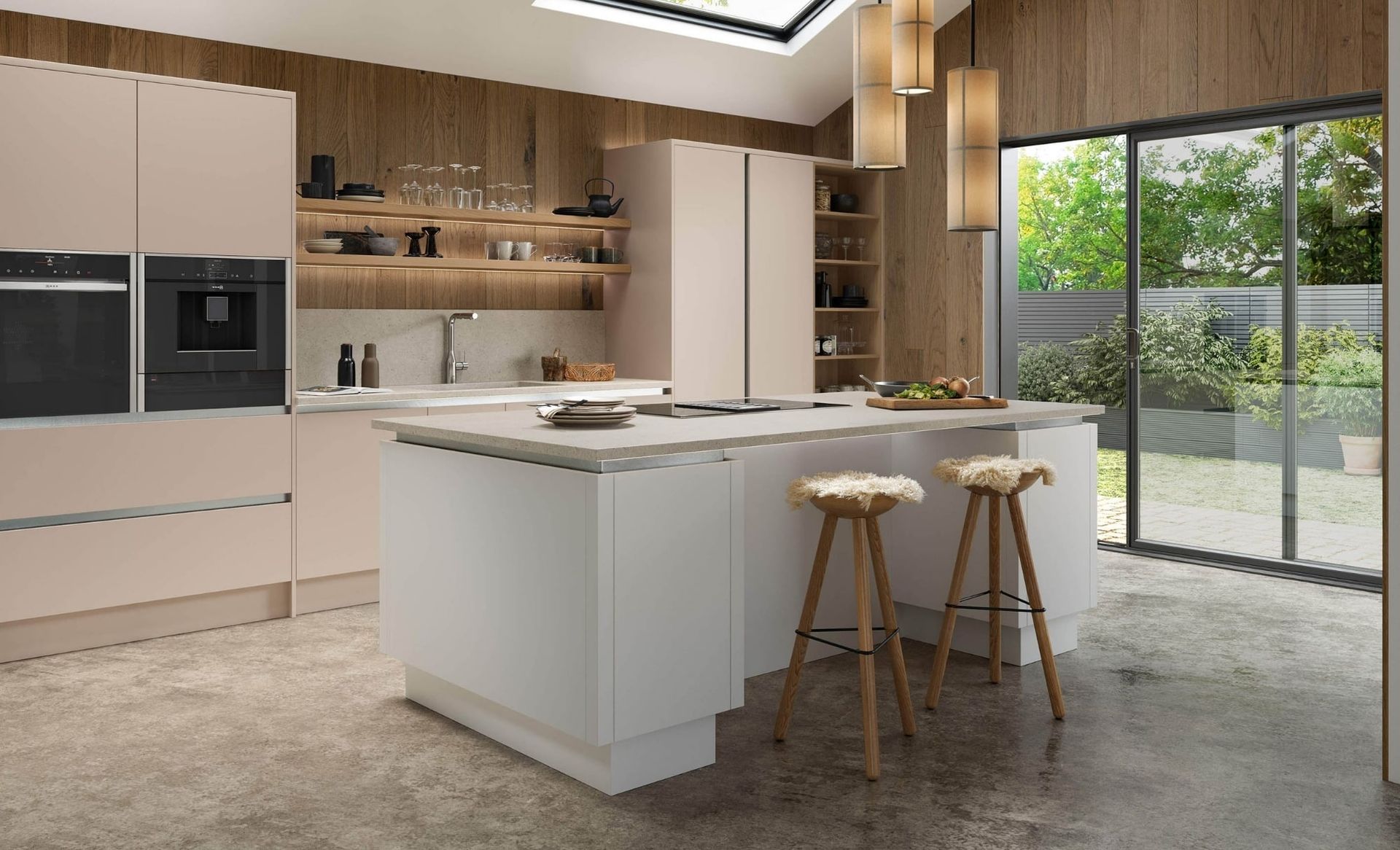 A modern kitchen with blush-pink cabinets, a white center island with two bar stools, and wooden walls looking onto a patio.