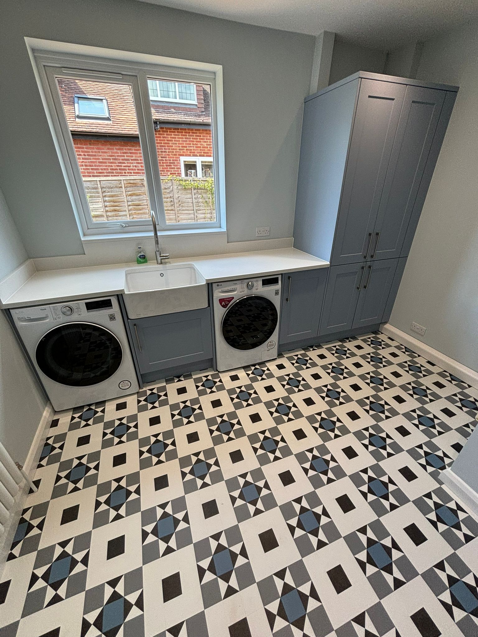 A laundry room with gray cabinets, two washing machines, a white sink, and patterned tiles on the floor.