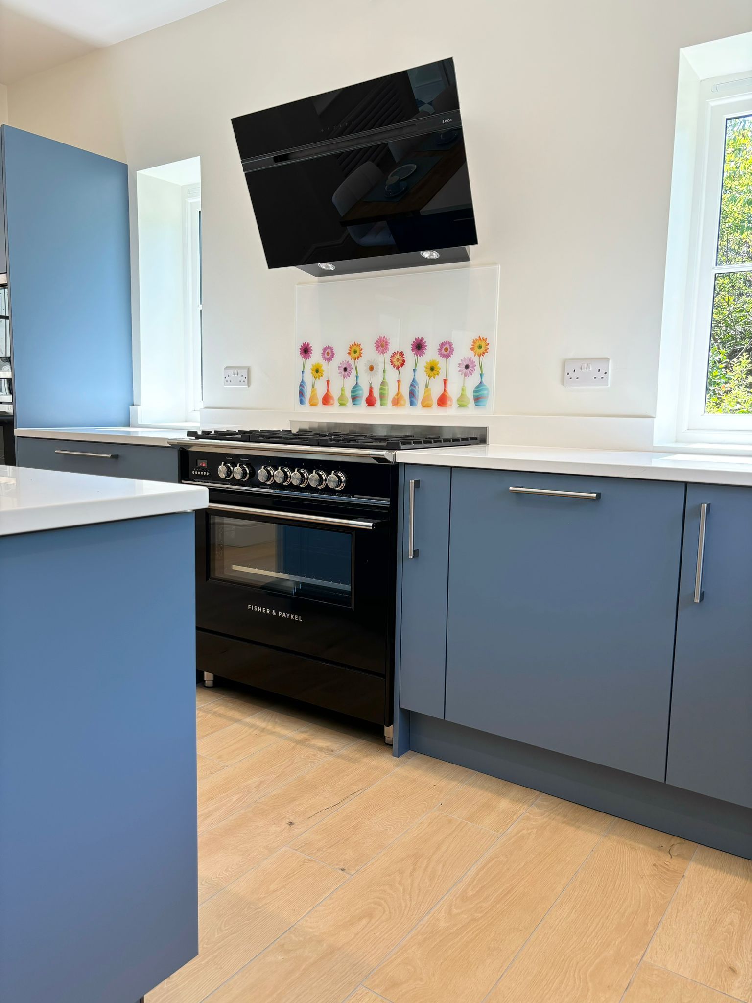 A modern kitchen featuring blue cabinets, white countertops, a black range cooker, and a floral-patterned splashback.