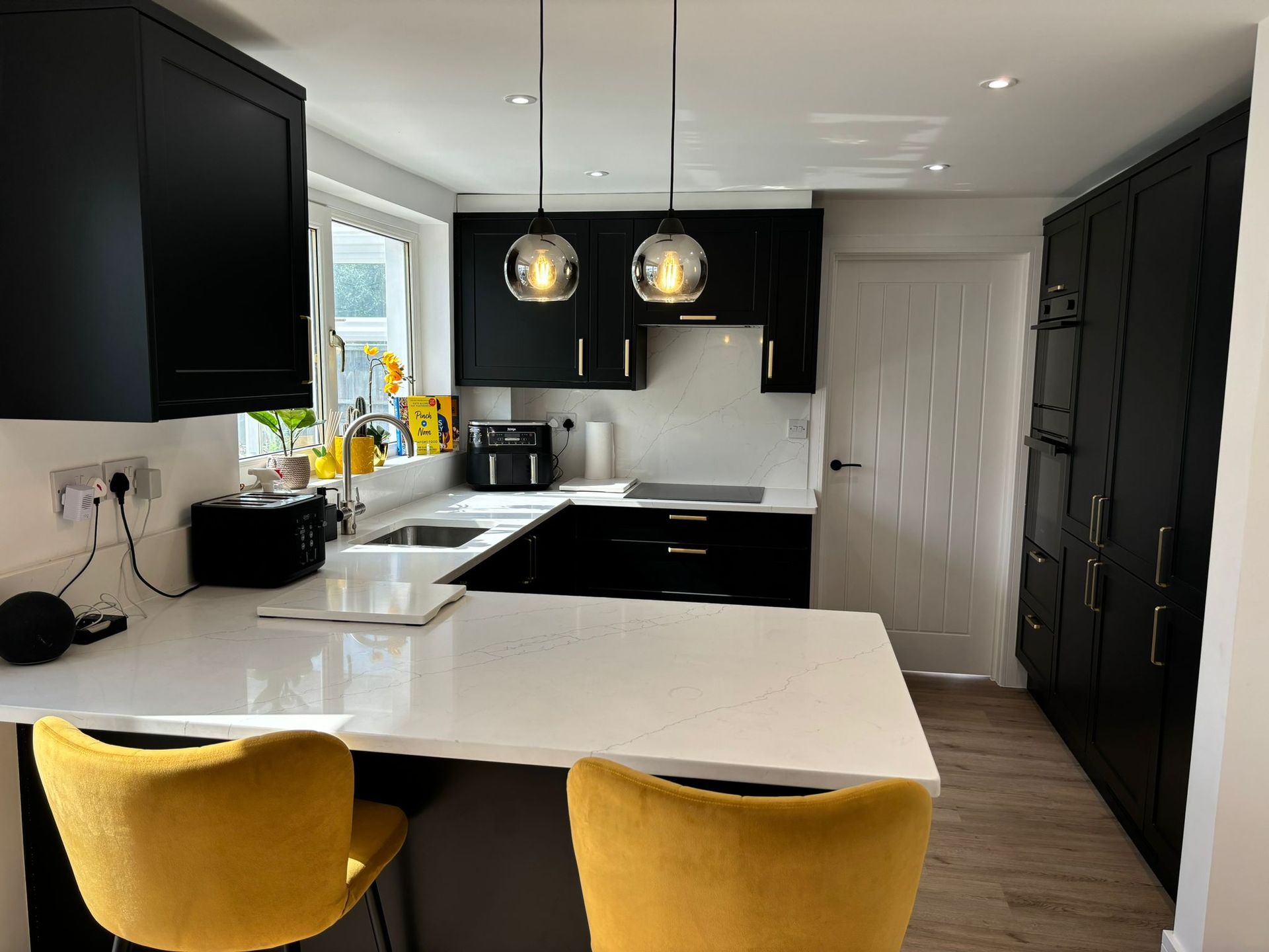 Modern kitchen with black cabinets, white countertops, two yellow bar stools, and two pendant lights.