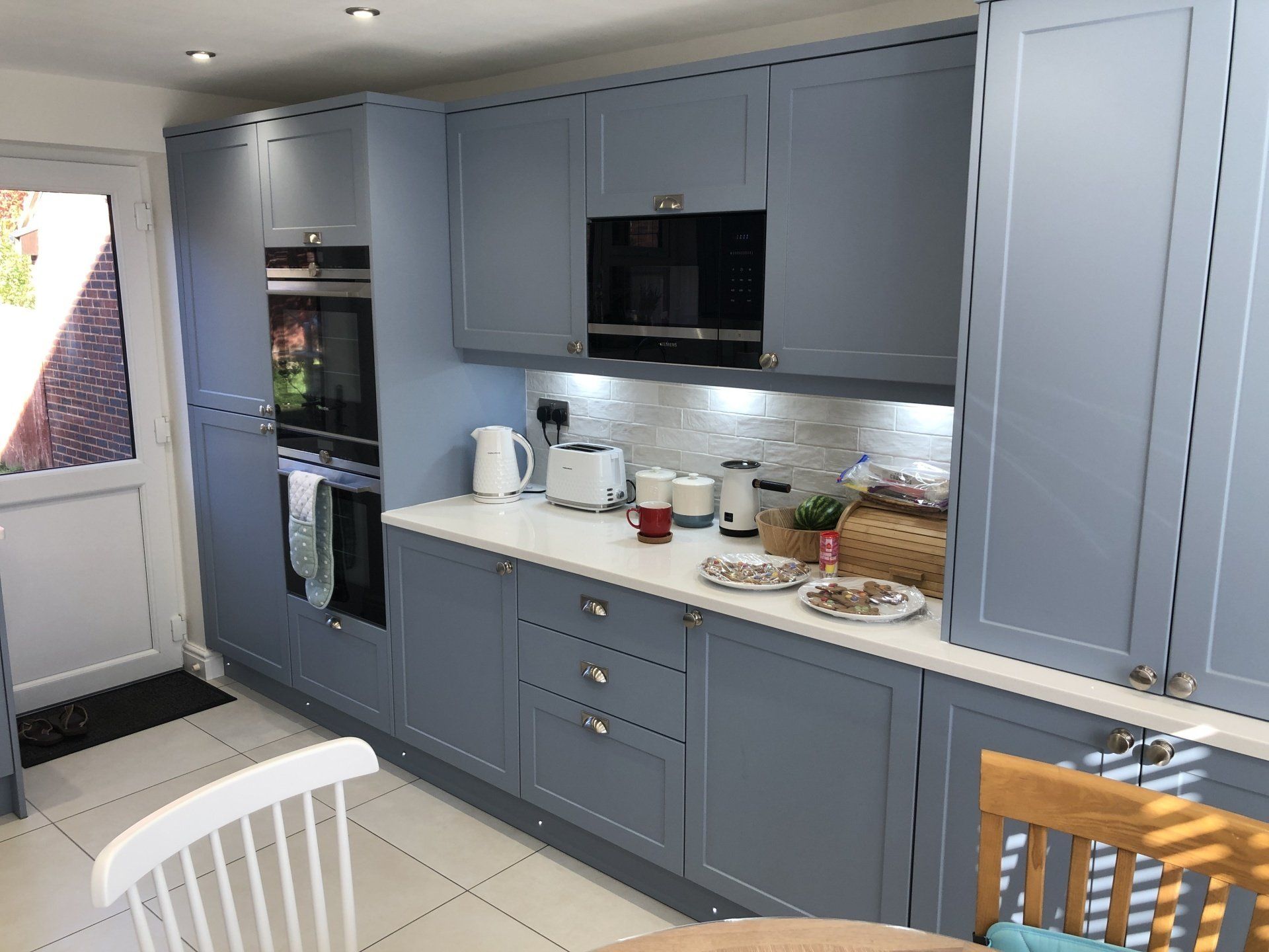 A modern kitchen featuring blue Shaker-style cabinets, white countertops, built-in appliances, and tiled flooring.