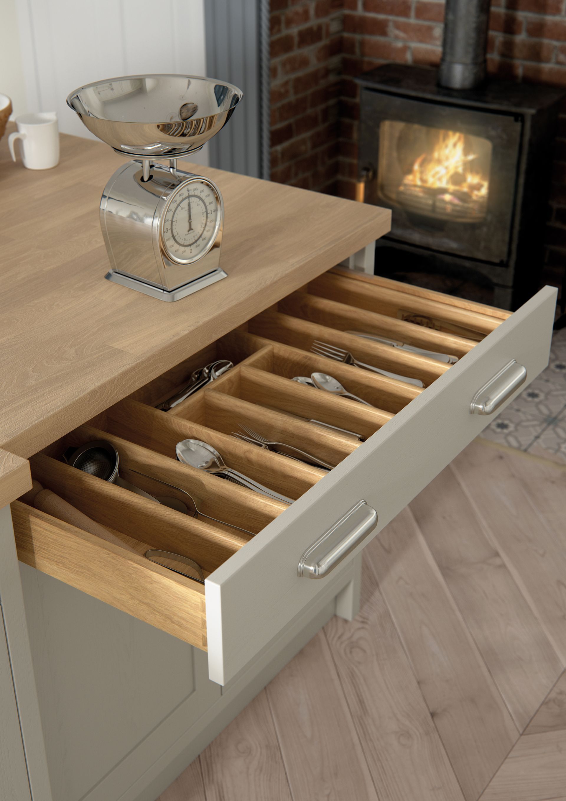 Open kitchen drawer with wooden dividers beside a lit wood stove and countertop decor