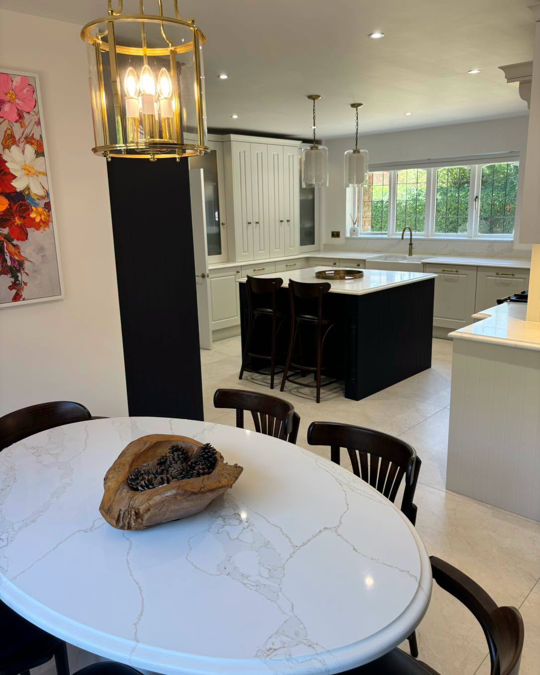 Modern kitchen and dining area with white marble table, black chairs, and an island near large windows